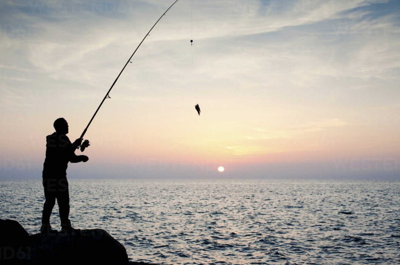 Silhouette of man fishing at sunset